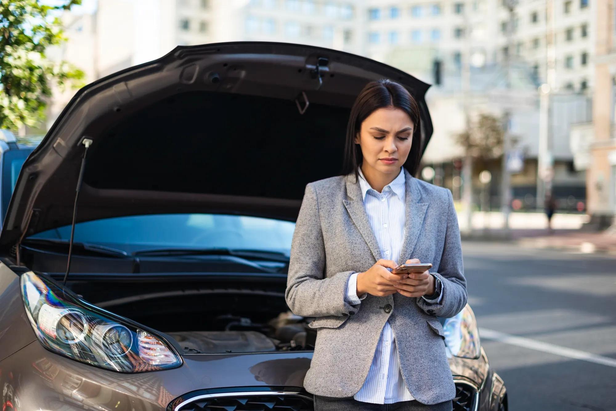 Une femme consulte son téléphone devant sa voiture, capot ouvert